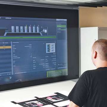 Großer Bildschirm von Offsetdruckmaschine, Mensch steht davor und bedient die Technik, Druckerei Hamburg
